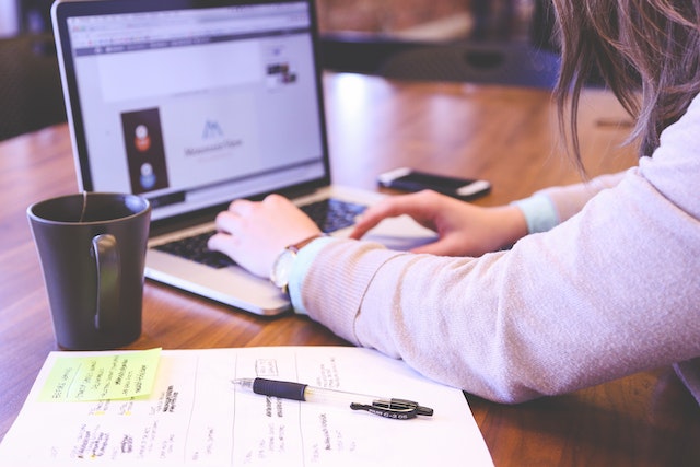 eine Person, die mit einem Laptop arbeitet, mit Notizbuch, Stift und Tasse auf dem Tisch